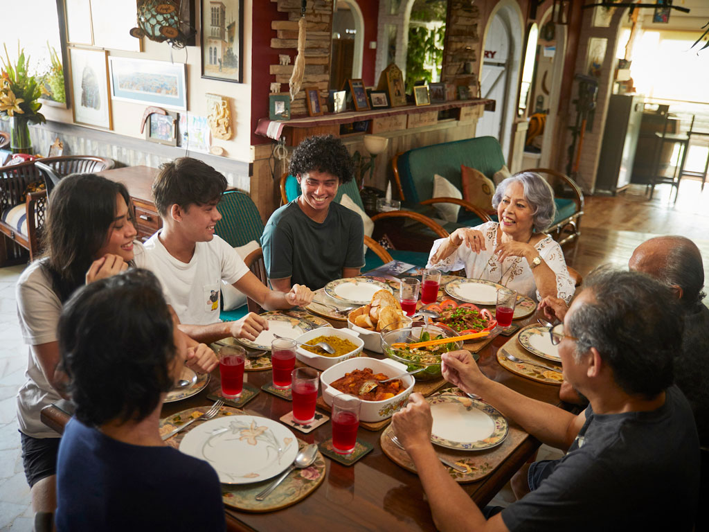 A family gathering around a dinner table, sharing food and drinks in a cozy home setting.